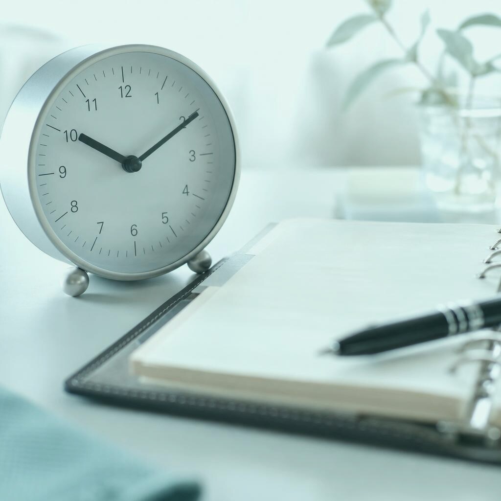 Analog clock beside an open diary conveying client follow-ups and long sales cycles